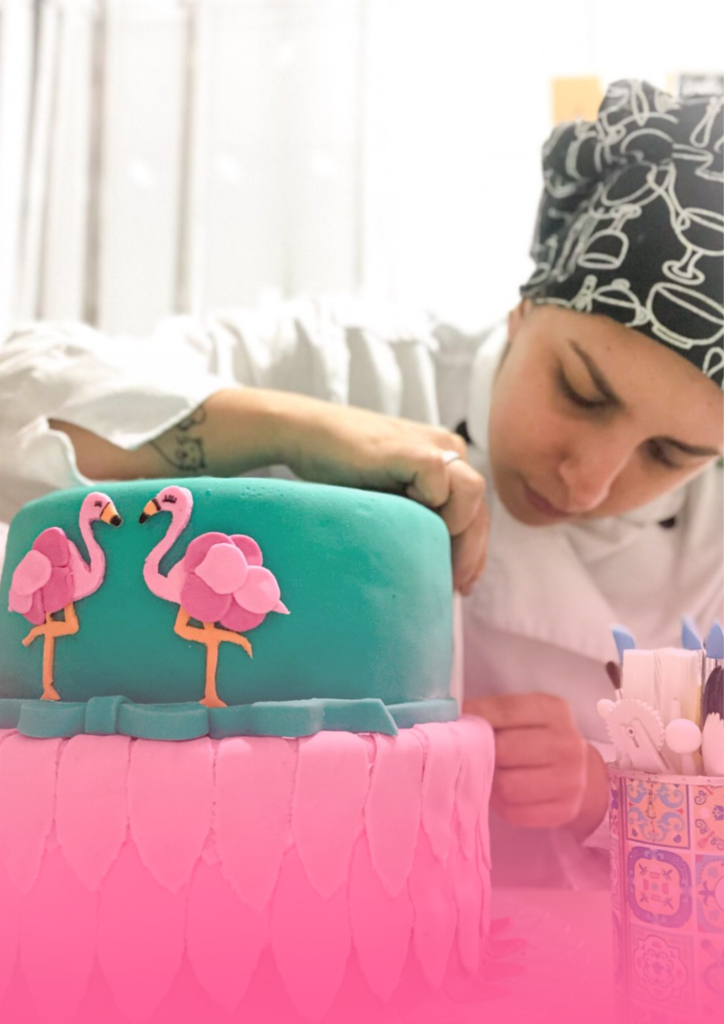 Confeiteira finalizando a decoração de um bolo com flamingos em pasta americana